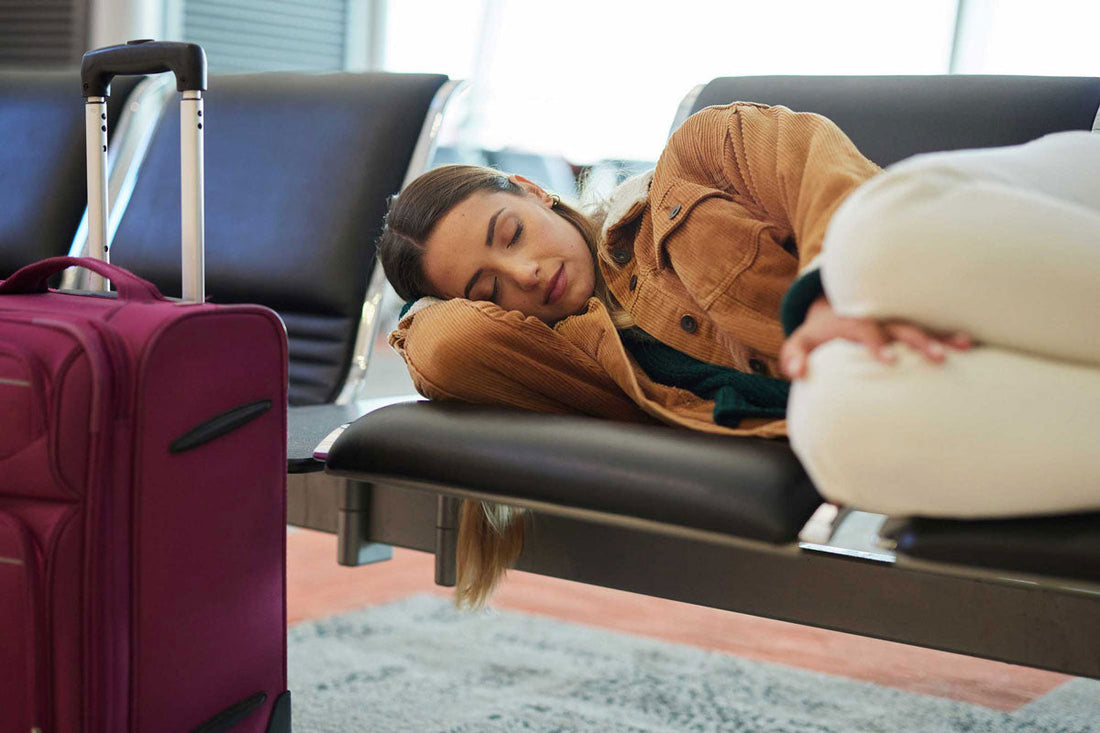 Eine Frau schläft auf einer Sitzbank am Flughafen, ihr Koffer steht vor ihr