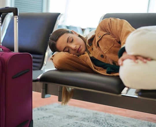 Eine Frau schläft auf einer Sitzbank am Flughafen, ihr Koffer steht vor ihr