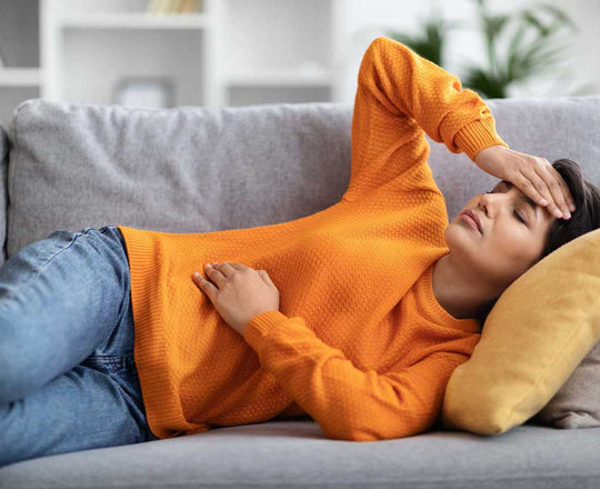 Eine Frau liegt auf einem Sofa und stützt ihren Kopf mit einer Hand, während sie mit der anderen ihren Bauch hält