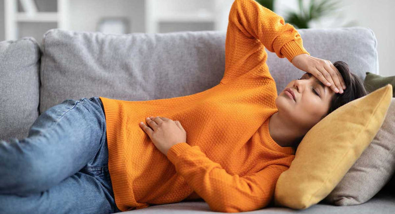 Eine Frau liegt auf einem Sofa und stützt ihren Kopf mit einer Hand, während sie mit der anderen ihren Bauch hält