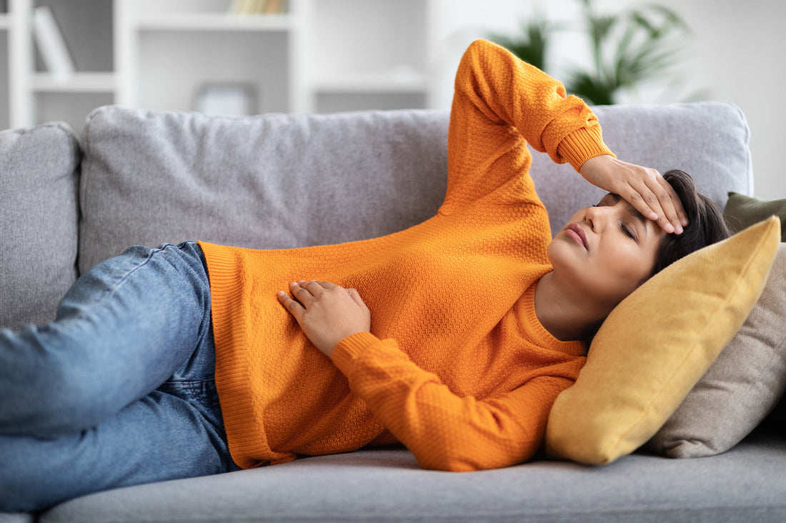 Geschwächte Frau hält sich den Bauch und den Kopf