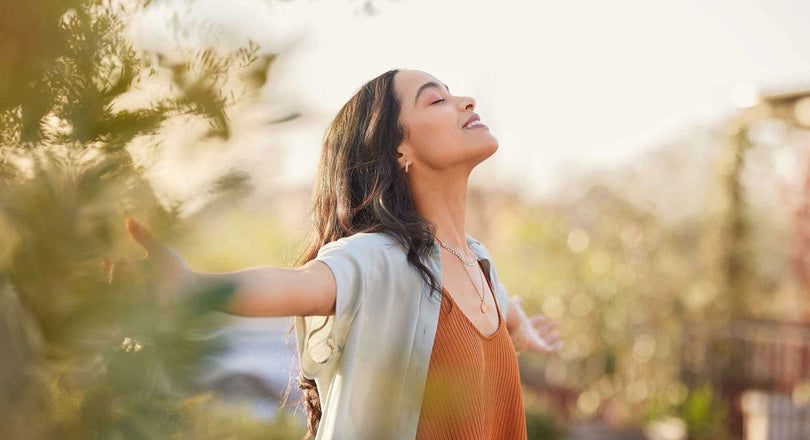 Eine Frau steht in der Natur mit weit ausgestreckten Armen und atmet tief durch