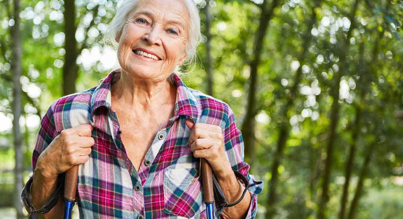 Ältere Frau spaziert mit Wanderstöcken im Wald