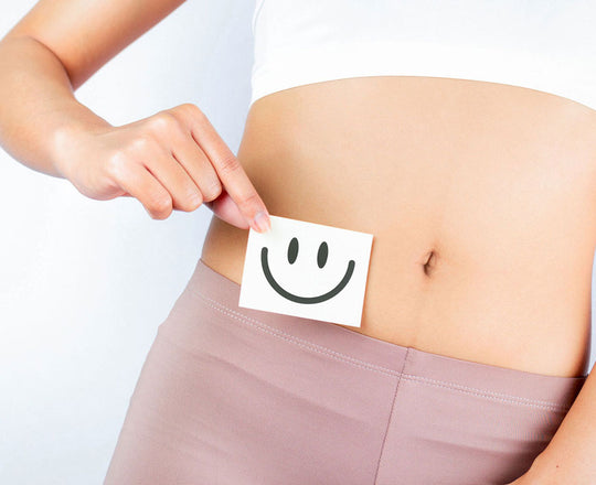 Frau hält einen Zettel mit einem lachenden Smiley vor ihrem Bauch