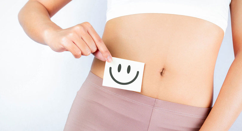 Frau hält einen Zettel mit einem lachenden Smiley vor ihrem Bauch