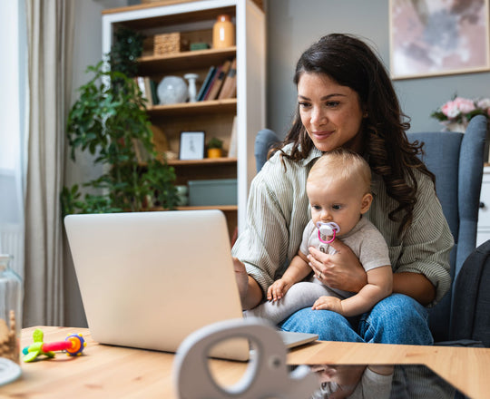Eine Mutter hält ihr Baby im Arm und arbeitet gleichzeitig an einem Laptop