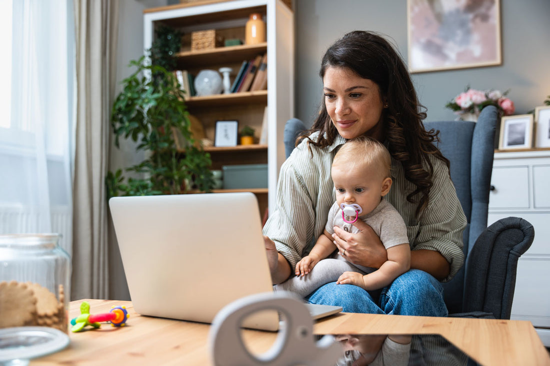 Eine Mutter hält ihr Baby im Arm und arbeitet gleichzeitig an einem Laptop
