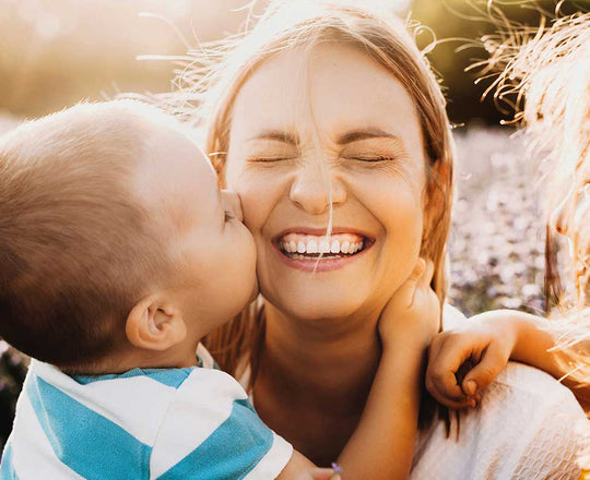 Frau wird von einem kleinen Kind umarmt und auf die Wange geküsst