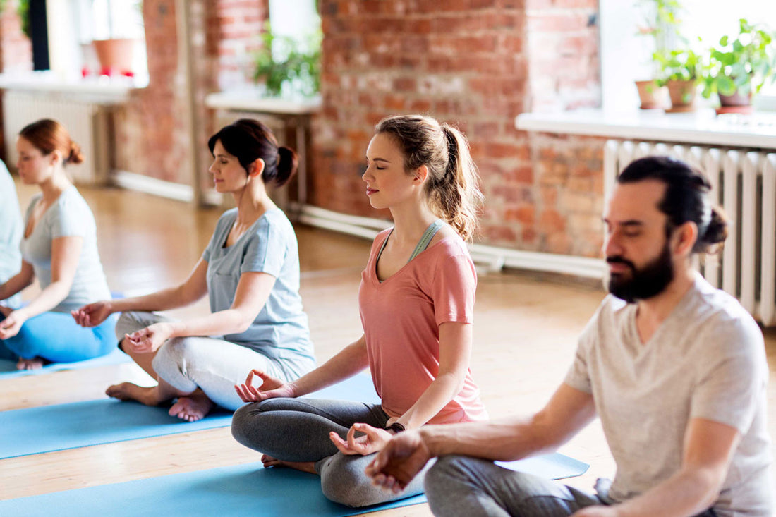 Drei Frauen und ein Mann sitzen im Schneidersitz beim Yoga