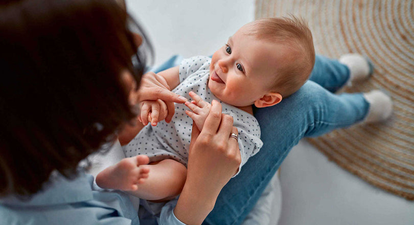 Baby liegt auf den Beinen seiner Mama und lächelt