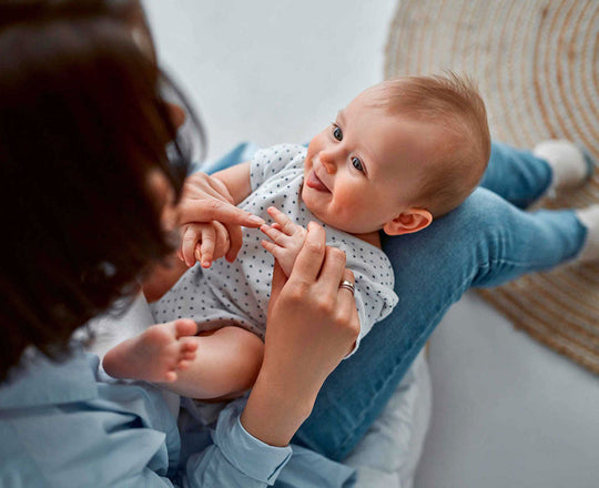 Baby liegt auf den Beinen seiner Mama und lächelt