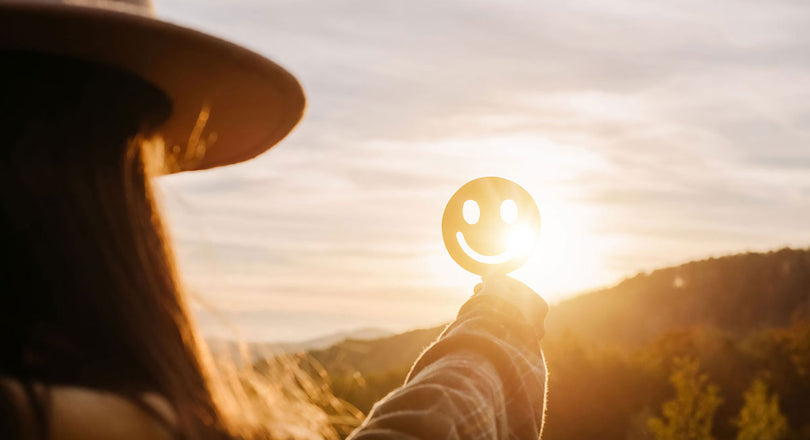 Frau hält ein lächelndes Gesicht gegen die Sonne