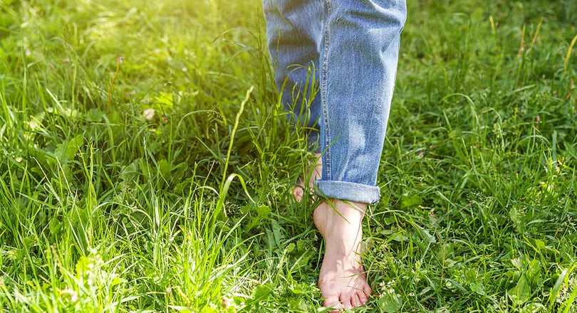 Frau läuft barfuß über eine grüne Wiese