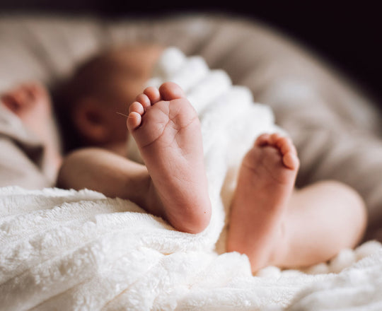 Baby liegt auf einem Polster und streckt die Füße in die Kamera