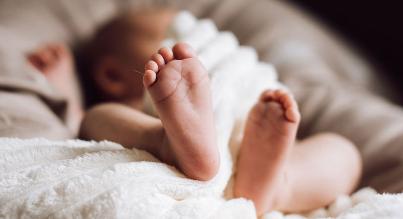 Baby liegt auf einem Polster und streckt die Füße in die Kamera