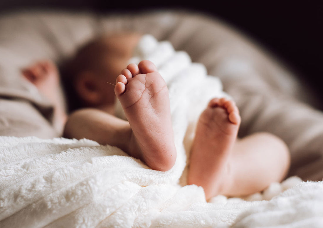 Baby liegt auf einem Polster und streckt die Füße in die Kamera