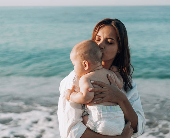 Eine Frau steht am Strand und hält ihr Baby am Arm