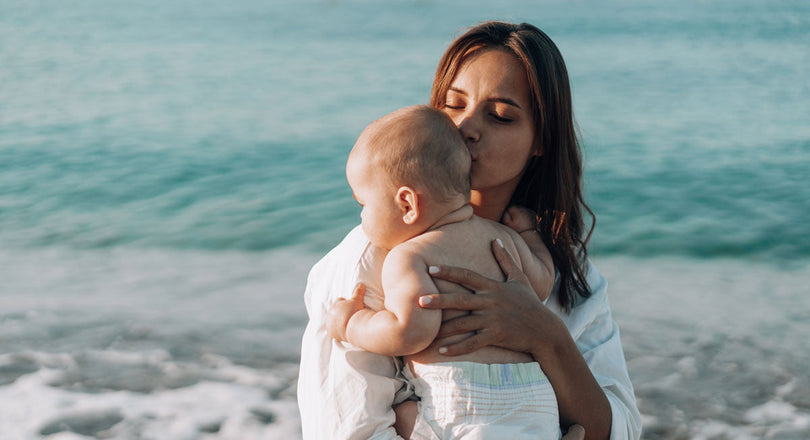 Eine Frau steht am Strand und hält ihr Baby am Arm