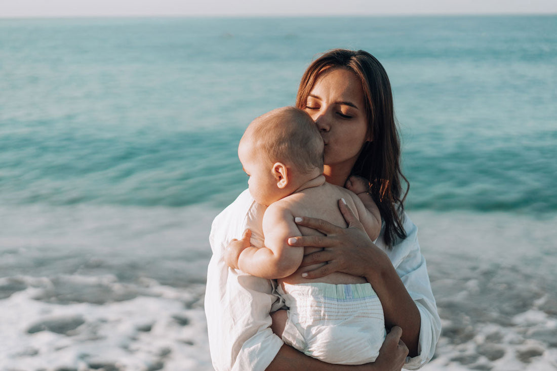 Eine Frau steht am Strand und hält ihr Baby am Arm