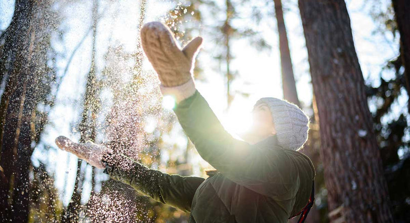 Frau steht im winterlichen Wald und wirft Schnee in die Luft