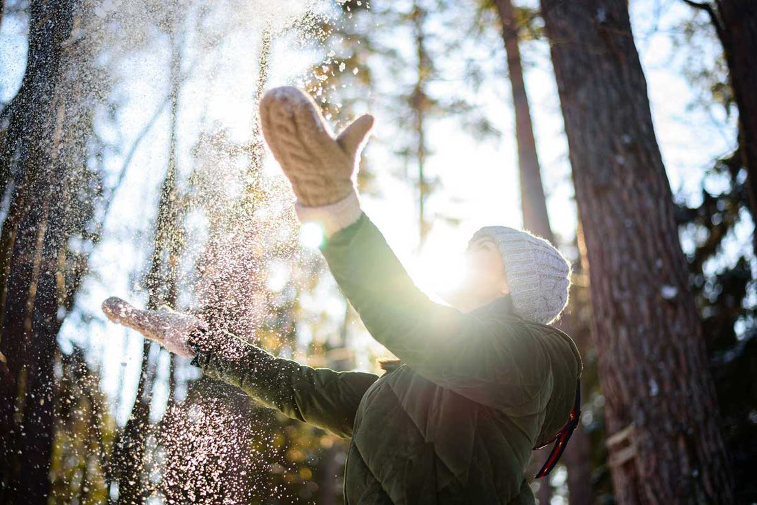 Frau steht im winterlichen Wald und wirft Schnee in die Luft
