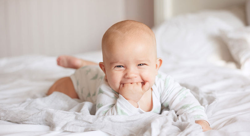 Baby liegt auf dem Bauch am Bett und knabbert an seiner Hand