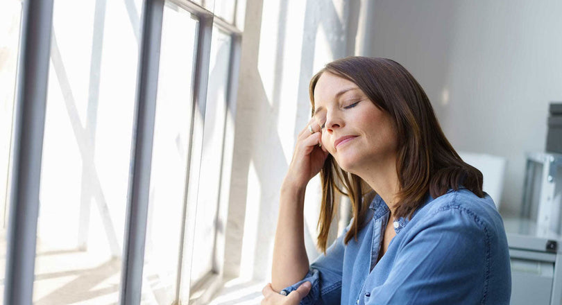 Eine Frau steht mit geschlossenen Augen vor einem Fenster