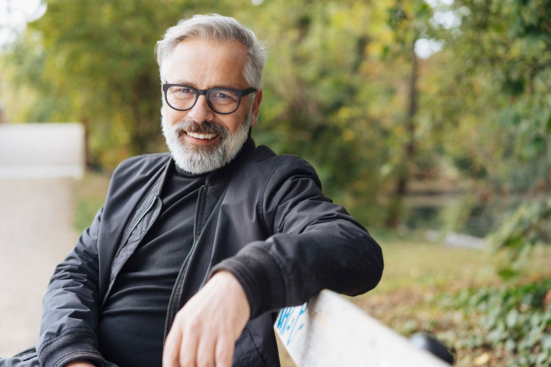 Mann sitzt auf einer Parkbank und lächelt in die Kamera