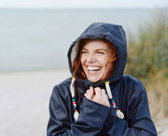 Frau mit Regenjacke steht am Strand
