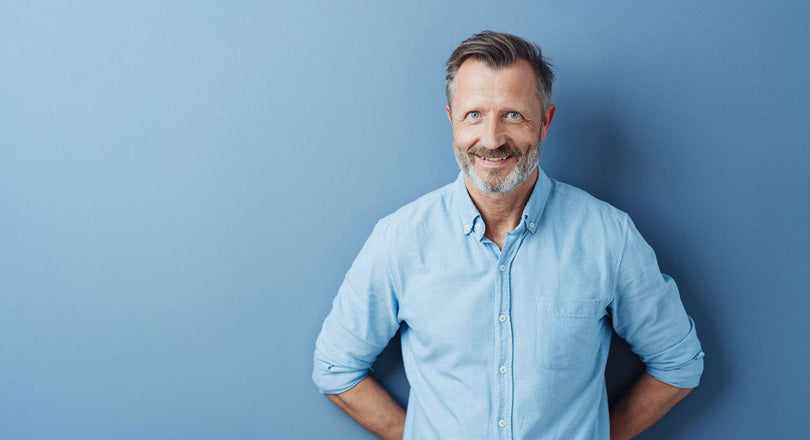 Mann steht vor einer blauen Wand und verschränkt die Hände hinter dem Rücken