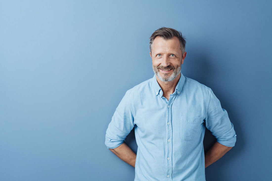 Mann steht vor einer blauen Wand und verschränkt die Hände hinter dem Rücken