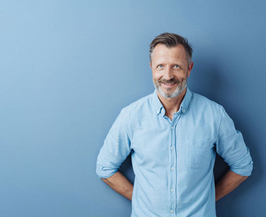 Mann steht vor einer blauen Wand und verschränkt die Hände hinter dem Rücken