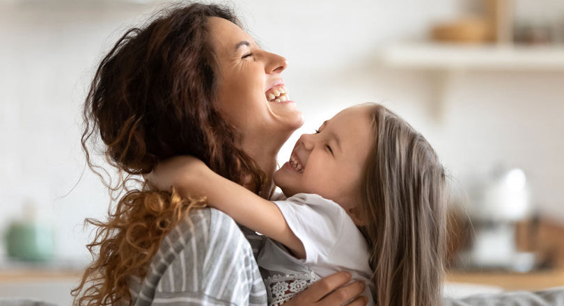 Ein Mädchen umarmt ihre Mama, beide lachen