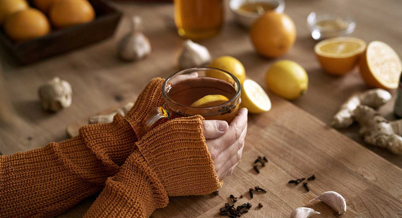 Frauenhände halten ein Glas mit Tee und Zitronenscheibe