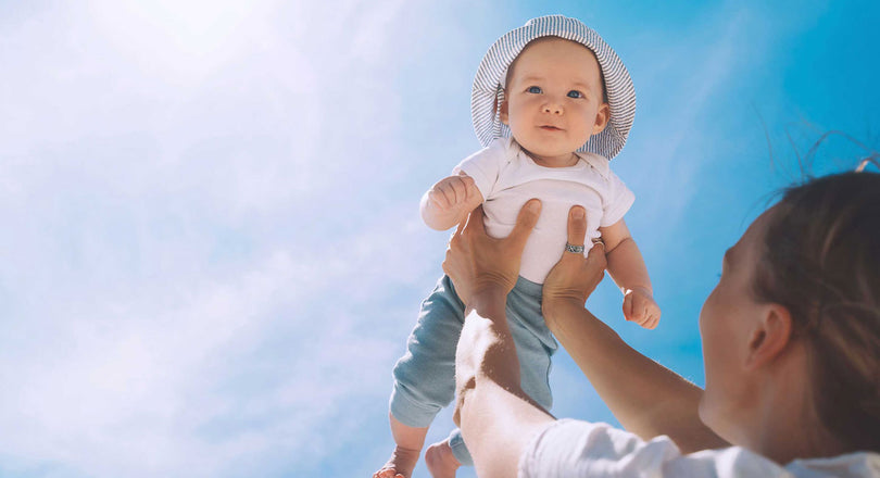 ine Mutter hält ihr Baby mit ausgestreckten Armen hoch in die Luft