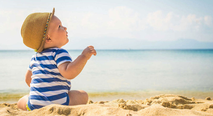 Baby sitzt im Sand am Strand