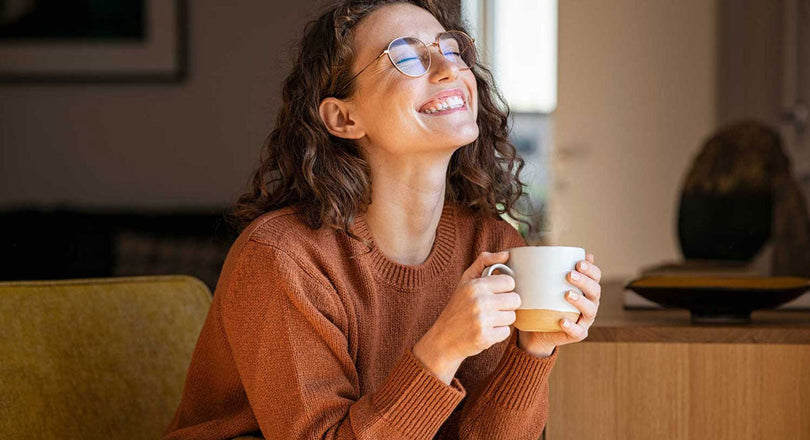 Frau sitzt mit einer Tasse auf dem Sofa und genießt die Sonne