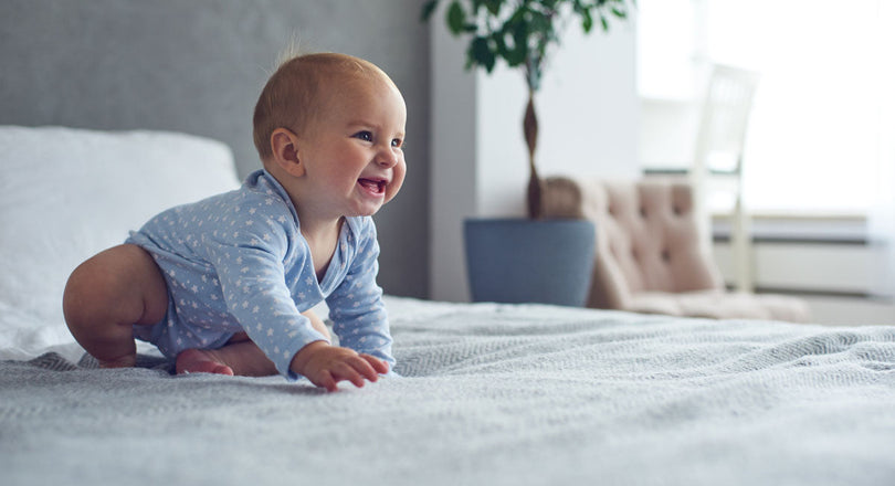 Krabbelndes und lächelndes Baby auf einem Bett