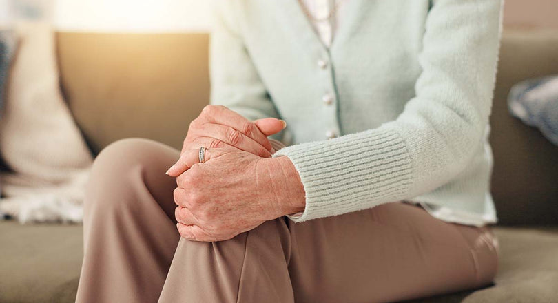 Frau, die sich mit beiden Händen ans Knie fasst, als hätte sie Schmerzen