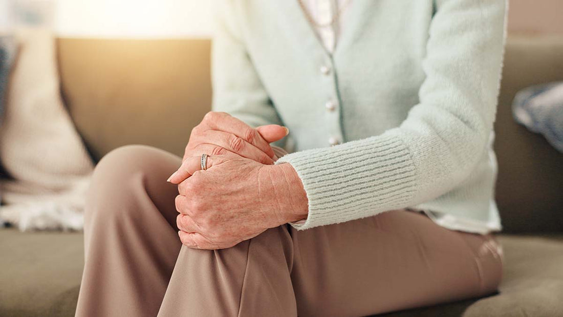 Frau, die sich mit beiden Händen ans Knie fasst, als hätte sie Schmerzen