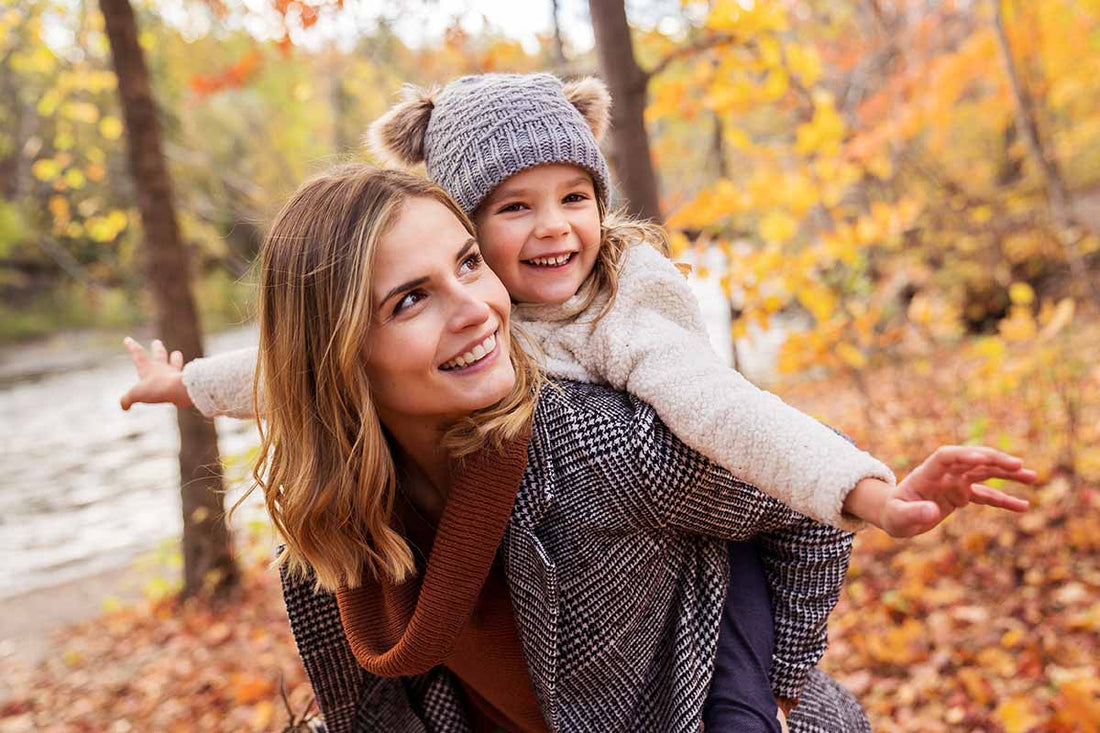 Mutter trägt ihre Tochter auf dem Rücken und geht durch einen herbstlichen Wald