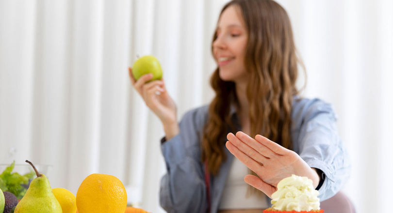 Frau schiebt einen Muffin zur Seite und hält einen Apfel in der Hand